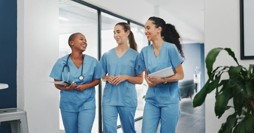 Three nurses in scrubs walking and talking together in a clinic corridor